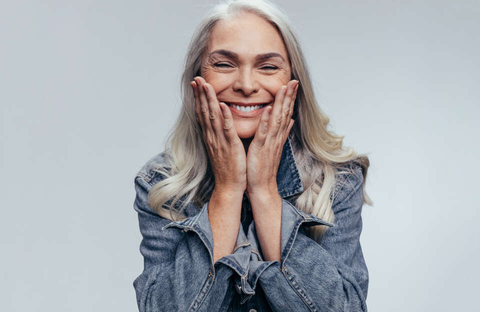 blonde women with white teeth smiling holding her face